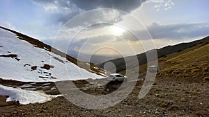 Two cars are parked high in the mountains on the pass. Beautiful mountain landscape. Snow-capped mountains, green hills and a