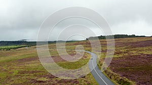 Two cars passing each other on road in countryside. Elevated view of landscape with grasslands and woods. Ireland