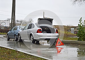 two cars and a red triangular sign at the scene of an accident on a wet road