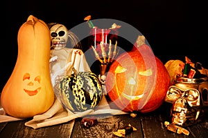 Two carved pumpkins with a cup of skeleton and a skull full of candy.