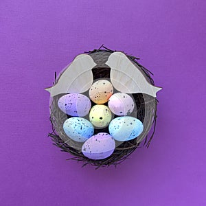 Two carved wooden birds and muticoloured Easter eggs in a bird nest