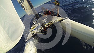 Two catamaran windsurfers sailing at high speed across sea, one tightening ropes