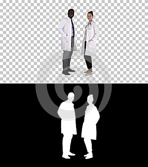 Two caucasian and afro american smiling doctors standing looking in to camera, Alpha Channel