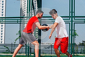 Two Caucasian basketball player fighting for ball possession at the basketball court on a sunny day