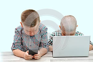 Two Caucasian boys ,brothers on a white isolated background. one plays in the phone,the other in the laptop. modern children and