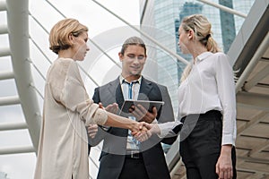 Two caucasian business woman having handshake to have greeting with caucasian businessman standing with tablet on hand