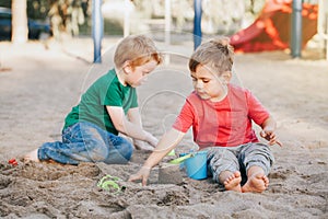 Two Caucasian children sitting in sandbox playing with beach toys. Little boys friends having fun together on playground. Summer