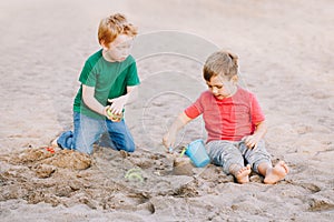 Two Caucasian children sitting in sandbox playing with beach toys. Little boys friends having fun together on playground. Summer