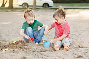 Two Caucasian children sitting in sandbox playing with beach toys. Little boys friends having fun together on a playground. Summer