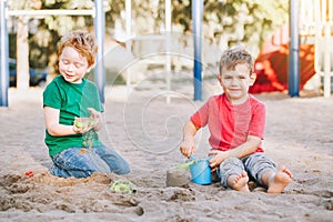 Two Caucasian children sitting in sandbox playing with beach toys. Little boys friends having fun together on a playground. Summer