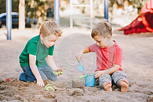 Two Caucasian children sitting in sandbox playing with beach toys. Little boys friends having fun together on a playground. Summer