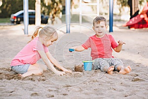 Two Caucasian children sitting in sandbox playing with beach toys. Little girl and boy friends having fun together on playground.