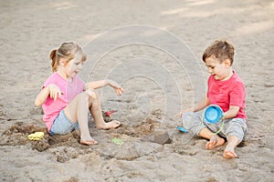 Two Caucasian children sitting in sandbox playing with beach toys. Little girl and boy friends having fun together on playground.
