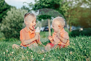 Two Caucasian funny children boys siblings sitting together eating sharing one ice-cream.
