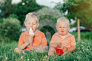 Two Caucasian funny children boys siblings sitting together eating sharing one ice-cream.