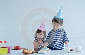 Two Caucasian kids little boy and girl enjoy eating birthday cake with hands at home on white background