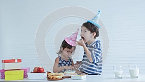 Two Caucasian kids little boy and girl enjoy eating birthday cake with hands at home on white background