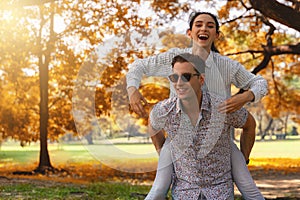 Two caucasian lover couple having romance moment in park together in autumn season. Boyfriend carrying his girlfriend on piggyback