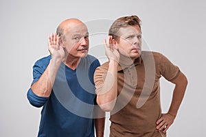 Two caucasian men hearing with hand on ear isolated on a white background. Please speak loudly.