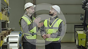Two Caucasian men standing at warehouse, talking and gesturing. Workers planning schedule at production site. Plant