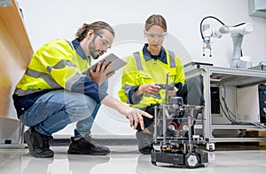 Two Caucasian professional technician or engineer workers sit on the floor and help to check and maintenance small robotic machine