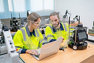 Two Caucasian professional technician or engineer workers sit in workplace and help to check and maintenance small robotic machine