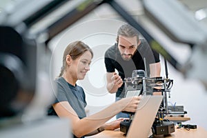 Two Caucasian professional technician or engineer workers sit in workplace and help to check and maintenance small robotic machine