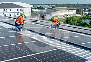 Two Caucasian technician workers sit on rooftop area to check and maintenance the solar cell panels on rooftop of factory or the