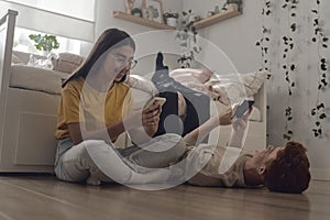 Two caucasian teenager lying at the floor in room and using mobile phones