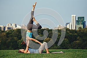 Two Caucasian women doing yoga stretching workout in park outdoors at sunset