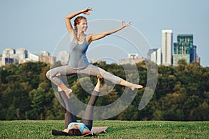 Two Caucasian women doing yoga stretching workout in park outdoors at sunset