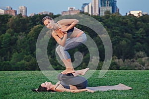 Two Caucasian women doing yoga stretching workout in park outdoors at sunset