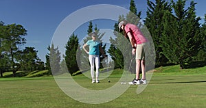 Two caucasian women playing golf one taking shot from bunker