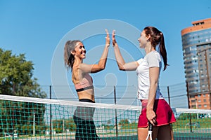 Two Caucasian women in sportswear greeting before a tennis match on an outdoor court. Players give a high five before