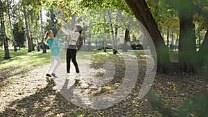 Two caucasian women tossing yellow leaves in the autumn park. Joyful family spending sunny day together. Positive young