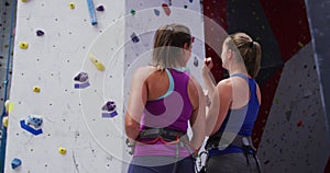 Two caucasian women wearing harnesses and talking at indoor climbing wall