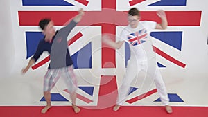Two caucasian young men synchronically dance and jump on background of british flag