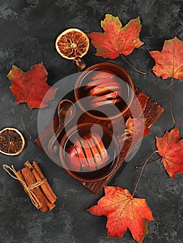 Two ceramic dark mugs with a hot autumn drink, mulled wine with apples and cinnamon and autumn fallen leaves on a rusty table,