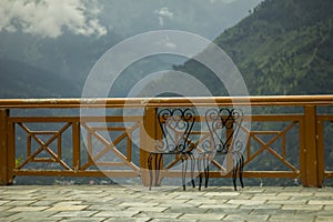 A two chairs on a balcony in the background of the mountains