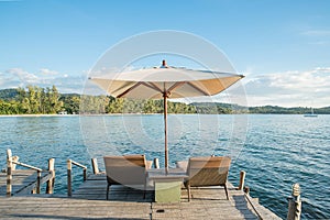 Two chairs beach and umbrella on wooden desk against blue sky.