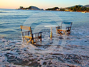 Two chairs and one table on the beach in the water. For all those who love to spend time at sea like this