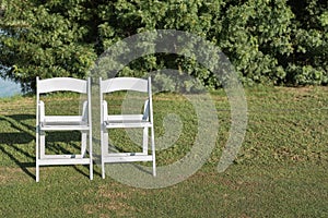 Two chairs placed on a green lawn set up for an outdoor wedding ceremony