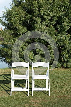 Two chairs placed on a green lawn set up for an outdoor wedding ceremony