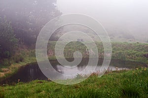 TWO CHAIRS ON A RIDGE OVERLOOKING A GREEN LANDSCAPE WITH A WATER HOLE IN FOREGROUND