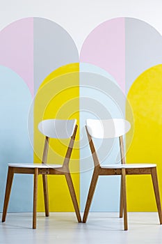 Two chairs set on a patterned wall with yellow accents in bright