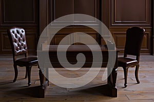 Two chairs sit opposite each other at a table in a dimly lit room, awaiting the presence of individuals engaged in a