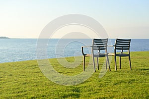 Two chairs stand on the grass next to the sea