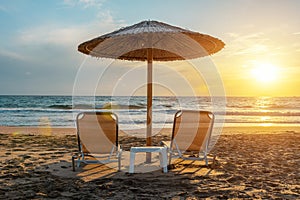 Two chairs under beach umbrella on tropical beach during sunset. Summer vacation concept