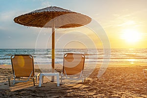 Two chairs under beach umbrella on tropical beach during sunset. Summer vacation concept