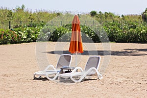 Two chaise lounges stand on the sand with a closed umbrella